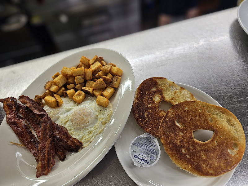 Classic breakfast plate with golden home fries, crispy bacon, eggs and toasted bagel at Maria's Breakfast and Lunch